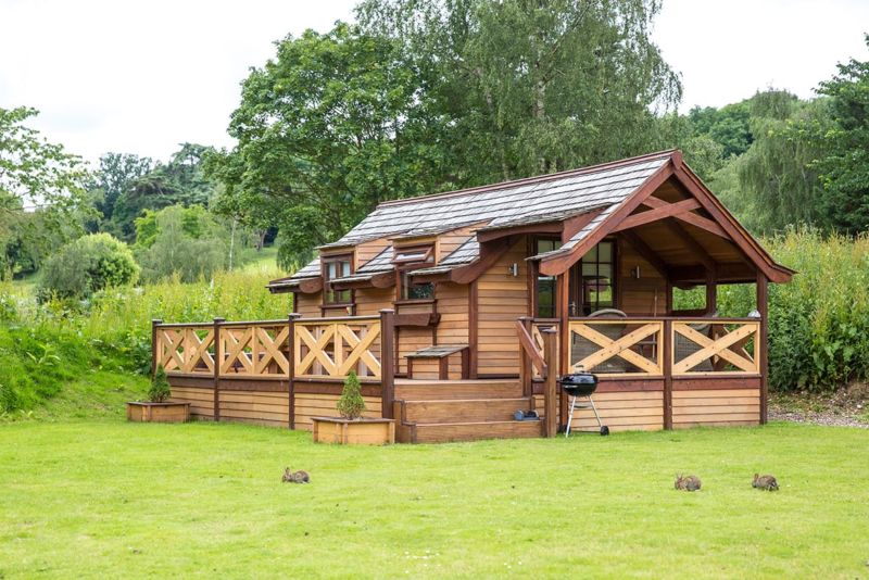 a glamping cabin that is wooden built with a small veranda around