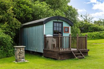 3 horse shoes converted shepherds hut, a sage green hut with dark wood decking in front