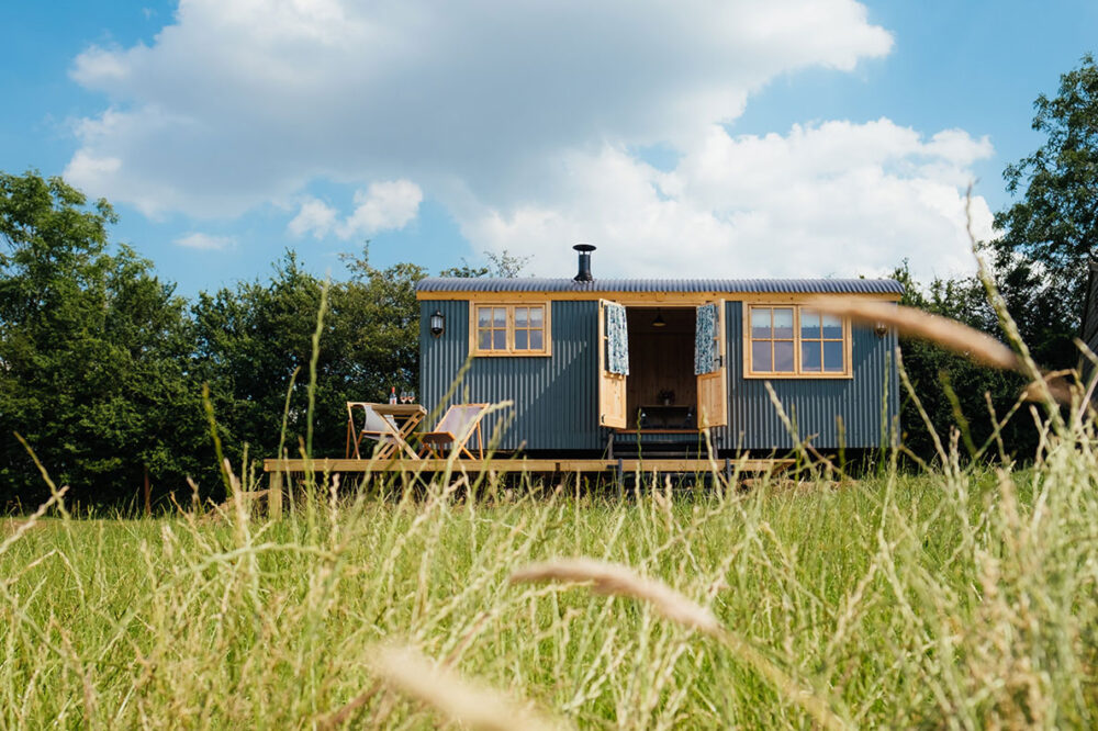 Hilltop Hideaway a deep green metal shepherds hut with light brown wooden windows. There is a small decking area to the front.