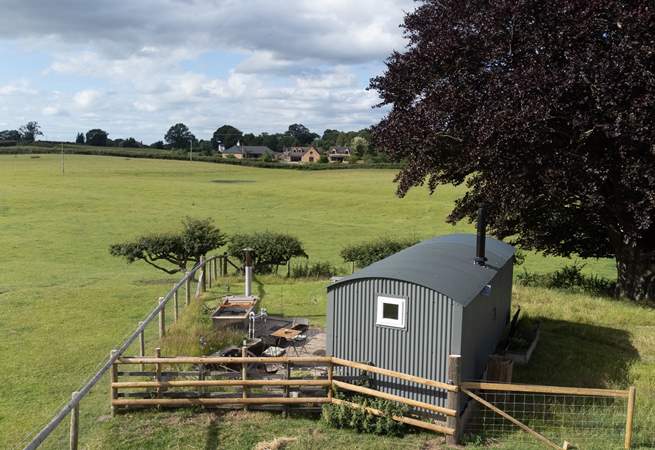 a shepherds hut set in the corner of a field there is an outdoor hot tub