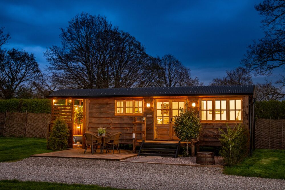 an extended luxury shepherds hut, made from wood with a rounded roof. It is light up from the inside